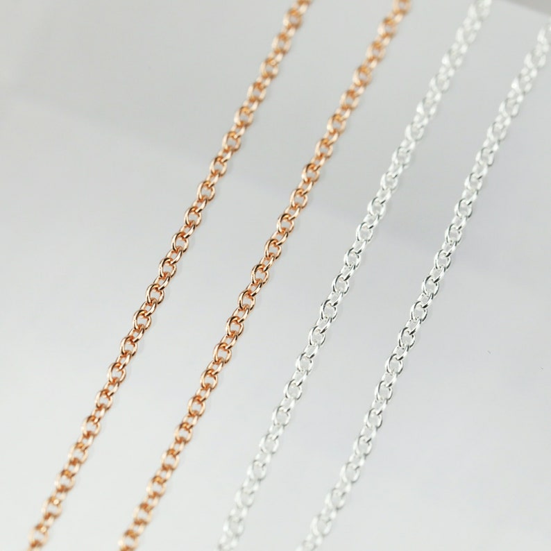 May include: Three chains of different metals: gold, rose gold, and silver. The chains are laid out in parallel lines on a white background.