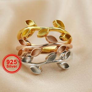 Pode incluir: Três anéis com design de folhas em ouro, ouro rosa e prata. Os anéis estão empilhados, mostrando os diferentes acabamentos metálicos. O anel de prata tem um círculo vermelho com o texto "925 Silver".