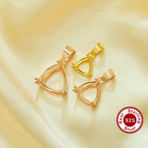 May include: Three sterling silver pendant settings in gold tones. The settings are triangular with prongs for holding a gemstone. The pendants are displayed on a gold satin fabric. A "Real 925 Sterling Silver" seal is visible.