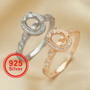 May include: Two silver rings with oval settings and a row of small clear stones around the settings. The ring on the left is silver, and the ring on the right is rose gold. The text "925 Silver" is in a red circle.