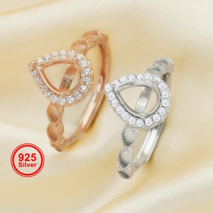 May include: Two silver rings with teardrop-shaped settings, one with a rose gold finish. Both rings are adorned with a halo of small, clear stones.