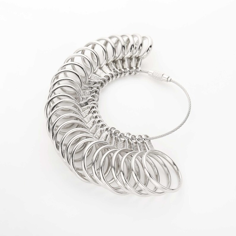 May include: A silver ring sizer with a chain and multiple rings of different sizes. The rings are arranged in a semi-circle shape.