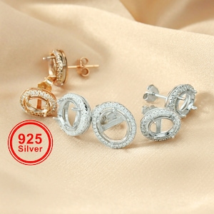 May include: A pair of silver oval-shaped earring settings with a row of clear cubic zirconia stones around the perimeter. The earrings are 925 silver.