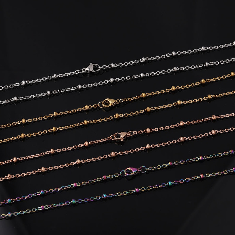 May include: A set of six delicate beaded chains in various colors, including silver, gold, rose gold, and rainbow. The chains are all the same length and have a lobster clasp closure.