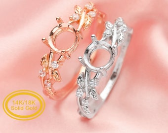 May include: Two rings with a delicate leaf and vine design. The ring on the left is rose gold with clear stones, and the ring on the right is silver with clear stones. Both rings have a round setting for a stone. The text "14K/18K Solid Gold" is visible in the image.