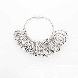 May include: A silver ring sizer with a chain and clasp. The sizer has a series of rings of different sizes.