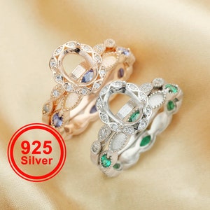 May include: Two silver rings with a delicate design. The top ring has a large oval setting with a halo of smaller stones. The bottom ring has a row of emerald green stones and a row of smaller stones.