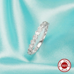 May include: A silver ring with a row of small, round, clear stones. The ring is on a light blue background. Real Sterling 925 Silver.