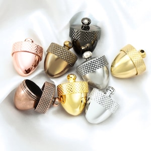 May include: Assortment of eight acorn-shaped charms in various metallic finishes, including gold, silver, copper, rose gold, and black. The charms have a textured, diamond-shaped pattern on the top and a smooth, rounded bottom.