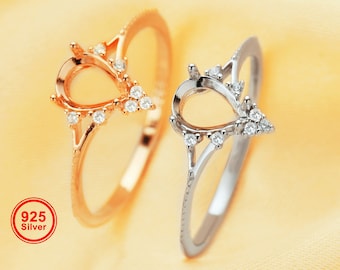 May include: Two silver rings with teardrop-shaped settings adorned with small clear stones. The rings are on a light yellow fabric background. 925 Silver.