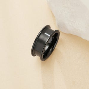 Könnte beinhalten: Ein schwarzer Ring mit abgeschrägter Kante und gebürsteter Oberfläche.