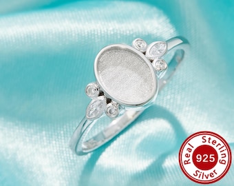 Op de afbeelding: Een zilveren ring met een ovale centrale zetting en decoratieve details. De ring heeft heldere, ronde en marquise-geslepen stenen. De ring is geplaatst tegen een lichtblauwe achtergrond. De ring is gestempeld met "Real Sterling 925 Silver".