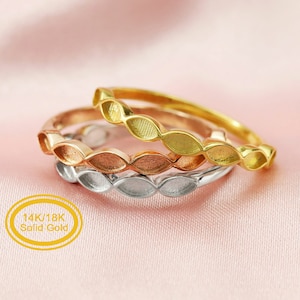 May include: Three gold rings stacked on top of each other. The top ring is yellow gold, the middle ring is rose gold, and the bottom ring is white gold. Each ring has a design of small, oval-shaped cutouts. The rings are labeled "14K/18K Solid Gold".