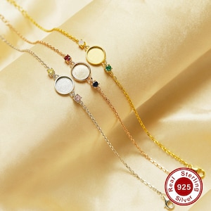 May include: Four silver chain bracelets with round, blank, silver-toned charms and colorful gemstones. The bracelets are on a gold background. The text "Real 925 Sterling Silver" is in red on a white circle.