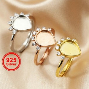 May include: Three silver rings with a teardrop-shaped bezel set with clear stones. The bezels are empty and ready to be filled with resin or other materials.