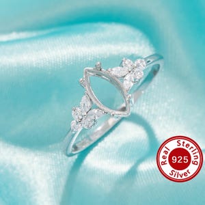 Könnte beinhalten: Ein Sterling Silber Ring mit einer marquiseförmigen Fassung, verziert mit floralen Designs und klaren Edelsteinen. Der Ring wird auf einem blauen Satinstoff präsentiert, mit einem rot-weißen "Real Sterling 925 Silver" Siegel.