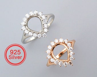 May include: Two teardrop shaped rings with a clear stone setting. The ring on the left is silver and the ring on the right is gold.