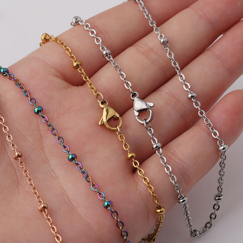 May include: Four different chain necklaces with small beads. The chains are silver, gold, rose gold, and rainbow.