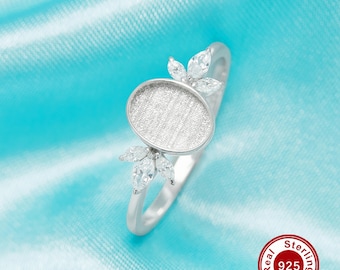 Op de afbeelding: Een zilveren ring met een leeg ovaal middenstuk en een ontwerp van kleine bladeren met heldere stenen. De ring ligt op een blauwe achtergrond met een rode cirkel waarop "Real Sterling 925 Silver" staat.