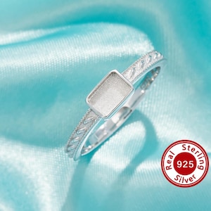 Peut inclure: Une bague en argent avec un sertissage rectangulaire. L'anneau de la bague présente un motif détaillé et texturé. La bague est présentée sur un tissu satiné bleu clair. La bague est estampillée "925 Silver".