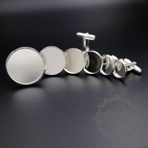 May include: A set of six silver cufflinks with round, smooth, blank surfaces. The cufflinks are arranged in a row from largest to smallest.