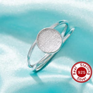 May include: A silver ring with a textured round center piece. The ring is made of sterling silver, as indicated by the "Real 925 Sterling Silver" label.