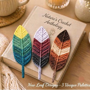 May include: Three crocheted leaf bookmarks resting on a book titled Nature's Crochet Anthology. The first leaf features yellow, green, and teal stripes. The second leaf has lavender, maroon, and dark gray stripes. The third leaf has brown, tan, and orange stripes.