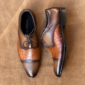 May include: A pair of brown leather oxford shoes featuring a textured ostrich-style pattern on the vamp, a smooth leather cap toe with decorative brogue perforations, dark brown laces, and the text FUTURE FEET printed on the inner sole.