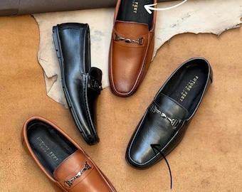 May include: Four loafers in black and tan leather with metal horsebit hardware. The tan loafers feature a textured finish, while the black loafers have a smooth surface. Each shoe has a black insole labeled Future Feet Premium.