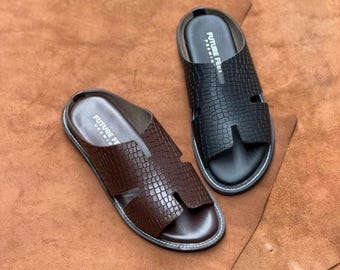May include: A pair of slide sandals featuring a textured crocodile-embossed pattern on the upper strap. One sandal is dark brown and the other is black. Both feature an open-toe design, a flat sole with white stitching, and the text FUTURE FEET PREMIUM.