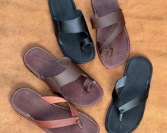 May include: Four pairs of flat sandals in black and brown leather. Two sandals feature a toe-loop design, while two feature a thong-style strap. Each footbed is embossed with the text FUTURE FEET PREMIUM FOOT WEAR and has visible stitching.