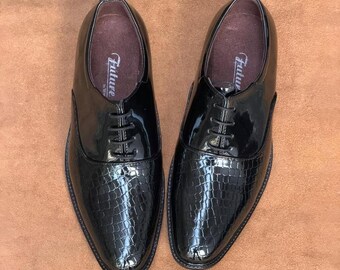 May include: A pair of black patent leather dress shoes with a textured crocodile-skin pattern on the toe and vamp. The shoes feature black laces, a rounded toe, and a dark brown interior lining with the word Future printed on the insole.