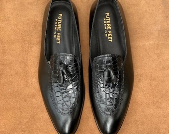 May include: A pair of black loafers featuring a textured crocodile-embossed leather vamp with a decorative tassel. The interior insole is black and printed with the gold text FUTURE FEET PREMIUM. The shoes have a smooth finish and pointed toe.