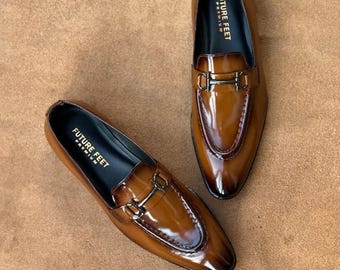 May include: A pair of glossy tan leather loafers featuring a dark brown gradient finish, a metallic horsebit detail across the vamp, and a black interior lining with the text FUTURE FEET PREMIUM printed in gold on the heel of the insole.