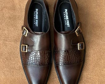 May include: A pair of dark brown leather double monk strap shoes featuring a textured crocodile-embossed panel across the midfoot, gold-toned metal buckles, and black insoles printed with the white text FUTURE FEET PREMIUM.