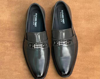 May include: A pair of dark grey glossy loafers featuring a metallic silver-toned bit across the vamp. The interior lining is dark grey with the text FUTURE FEET PREMIUM printed in white on the heel area of the insole of each shoe.