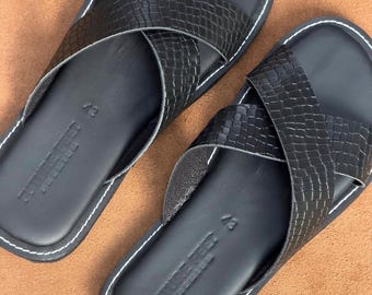 May include: A pair of black sandals featuring a crisscross strap design with a textured crocodile-like pattern. The footbed is smooth black with white contrast stitching along the edges and the text FUTURE FOOT PREMIUM 43 embossed on the heel.
