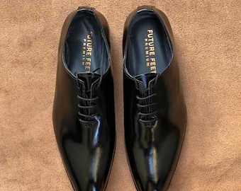 May include: A pair of black leather oxford shoes with a polished finish, thin black laces, and a pointed toe. The interior insole features the gold text FUTURE FEET PREMIUM printed clearly on the heel area of each shoe.