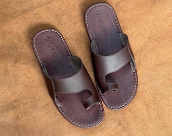 May include: A pair of dark brown leather toe-loop sandals featuring a wide strap across the top and a loop for the big toe. The footbed is stamped with the text FUTURE FEET PREMIUM FOOTWEAR and the edges are finished with visible white stitching.