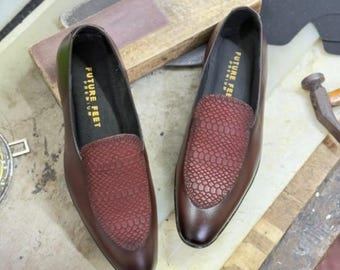 May include: A pair of dark brown leather loafers featuring a textured, reddish-brown snakeskin-patterned vamp. The interior black insole is clearly printed with the text FUTURE FEET PREMIUM in gold lettering. These slip-on shoes have a smooth finish.