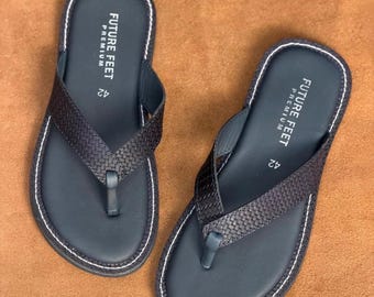 May include: A pair of dark gray flip-flops featuring a woven texture on the straps and white contrast stitching along the edges. The footbed displays the text FUTURE FEET PREMIUM and the number 42 printed in white on the heel area of each sandal.