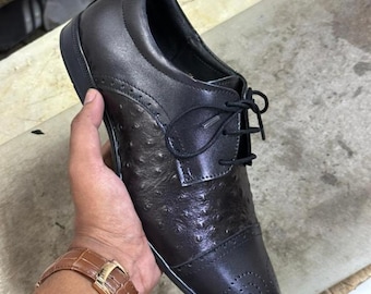 May include: A dark brown lace-up oxford shoe featuring a textured ostrich-style leather finish on the quarter and a smooth leather cap toe with decorative brogue perforations. The shoe includes black laces and a matching dark brown sole.
