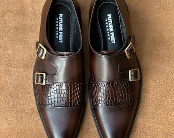 May include: A pair of dark brown double monk strap shoes featuring a smooth leather toe cap and a textured crocodile-embossed leather mid-section. Each shoe has two gold-toned metal buckles and an interior label reading FUTURE FEET PREMIUM.