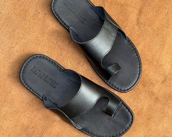 May include: A pair of black leather sandals featuring a toe loop design and a wide strap across the top. The footbed is embossed with the text FUTURE FEET PREMIUM FOOTWEAR. The sandals have visible stitching along the edges of the sole and strap.