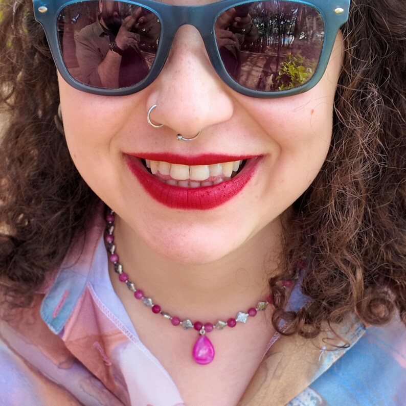Close-up over an open collar: the smooth pink teardrop hangs from a small metal bail, flanked by pea-sized round beads and stamped diamond spacers on either side.