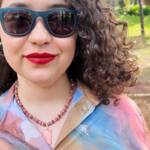 Worn front view: the beaded strand rests along the collarbone over a pastel printed shirt, with the gold-framed coral pendant hanging on the upper chest and gold rondelles catching daylight between the red beads.