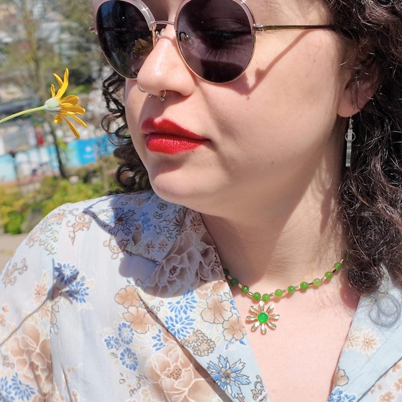 Daylight view from below: deep green round beads and small gold spacers curve around the neck, with the cream-and-gold daisy pendant and its green centre hanging at the top of the chest.