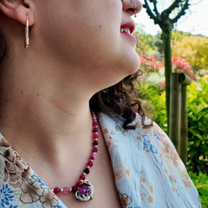 The strand curves under an open collar in sunlight, each round bead about the size of a small pea, with the filigree heart pendant hanging at the centre of the row.