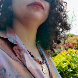 Outdoor shot of the necklace worn with an open printed shirt, the multicoloured 8 mm beads running along the collar line and the gold spiral pendant sitting at the centre of the chest.