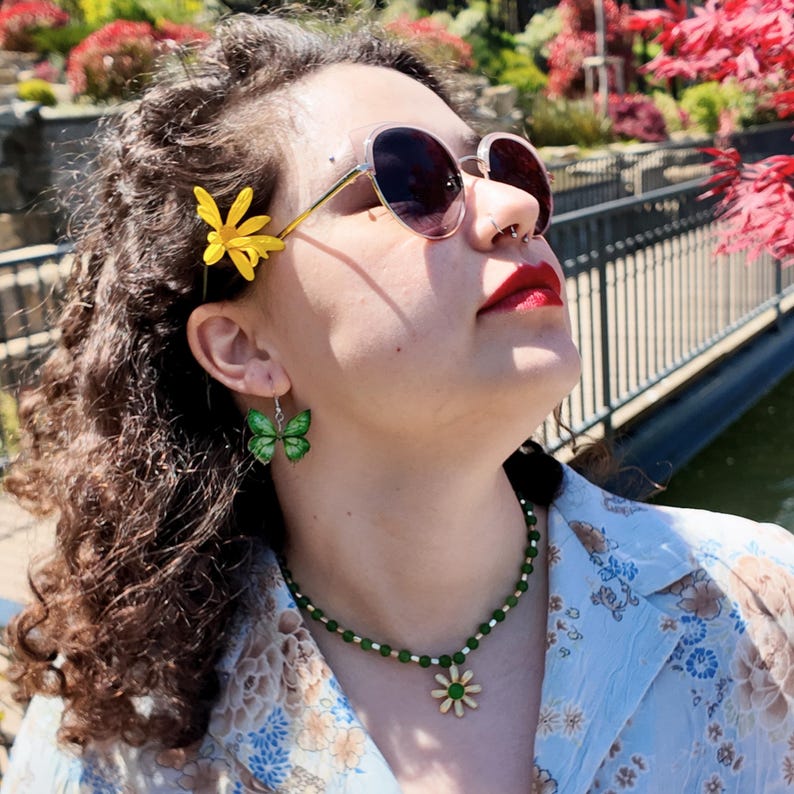 Side view in sunlight showing the short green bead strand following the curve of the neck, the small daisy pendant with its round green centre sitting low at the front.